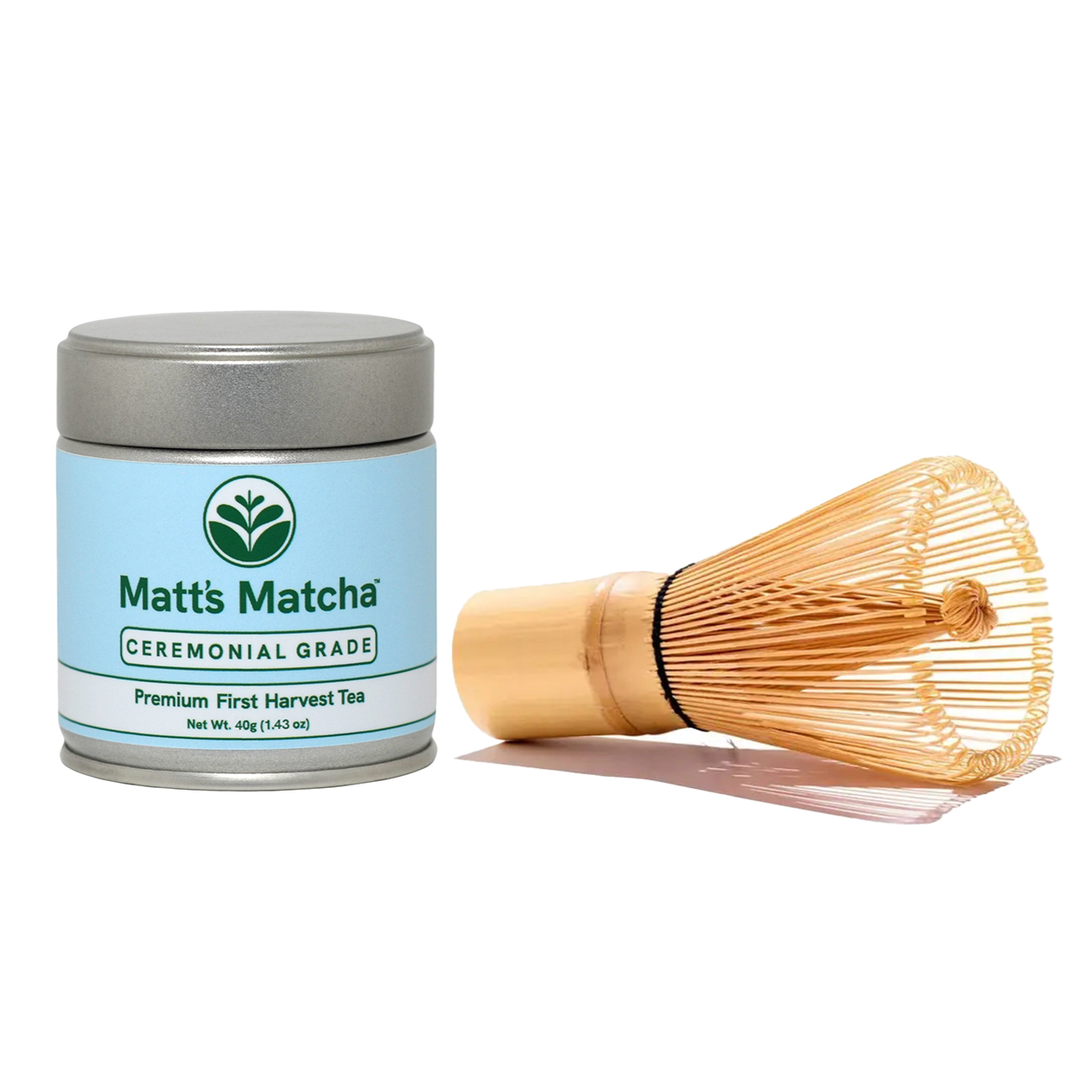 A sleek metal tin of matcha with a blue label featuring green 'Matt's Matcha' lettering next to a bamboo whisk laid on its side with a white background