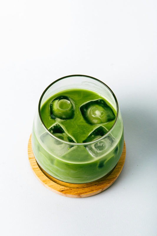 An iced matcha latte set on a wooden coaster with a white background.