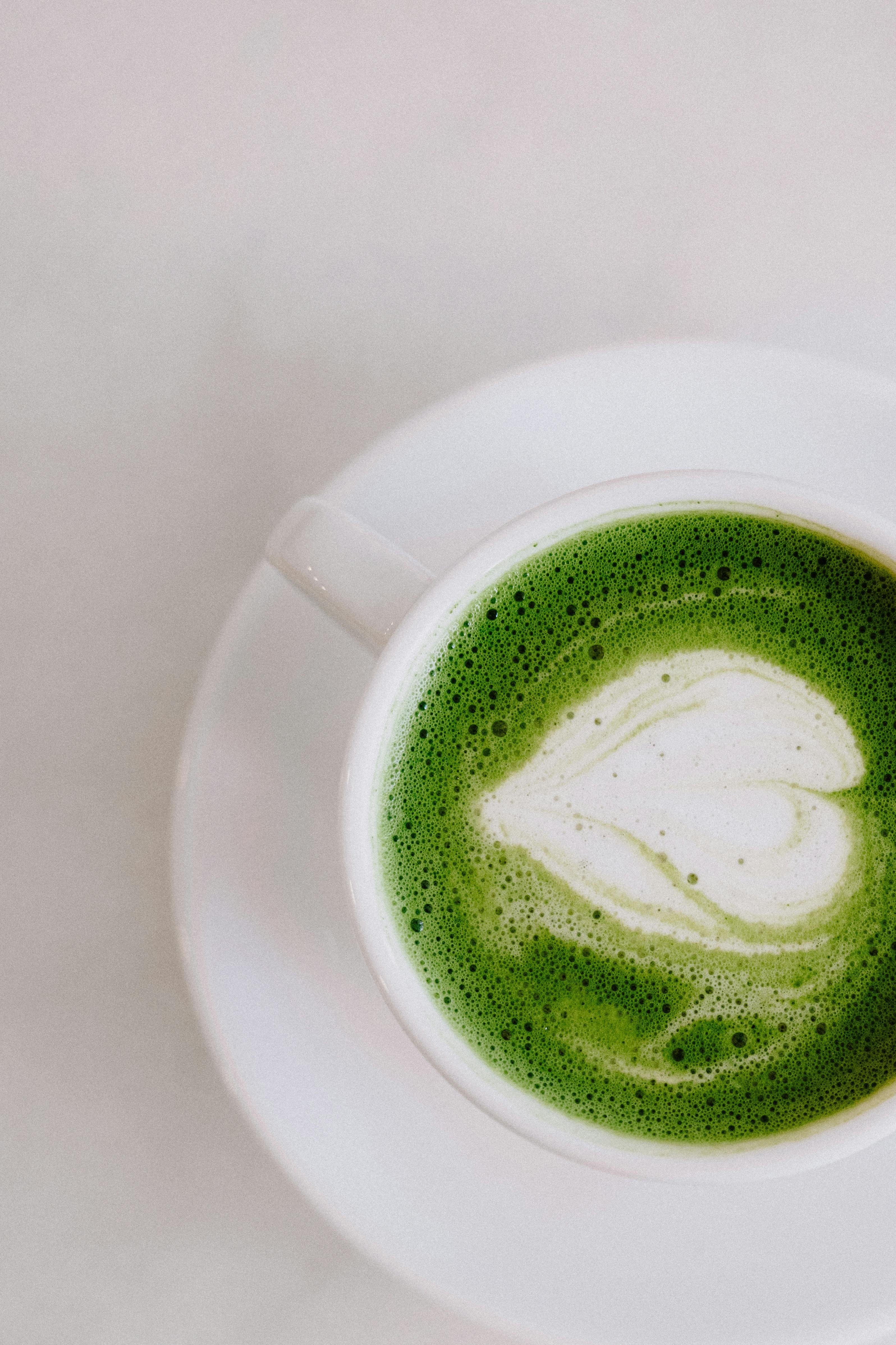 A hot green matcha latte with latte art in a white mug on a matching plate, set against a clean white background.